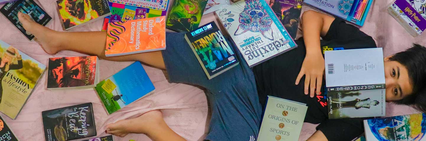 teen-events-banner Teen boy laying down and covered in books