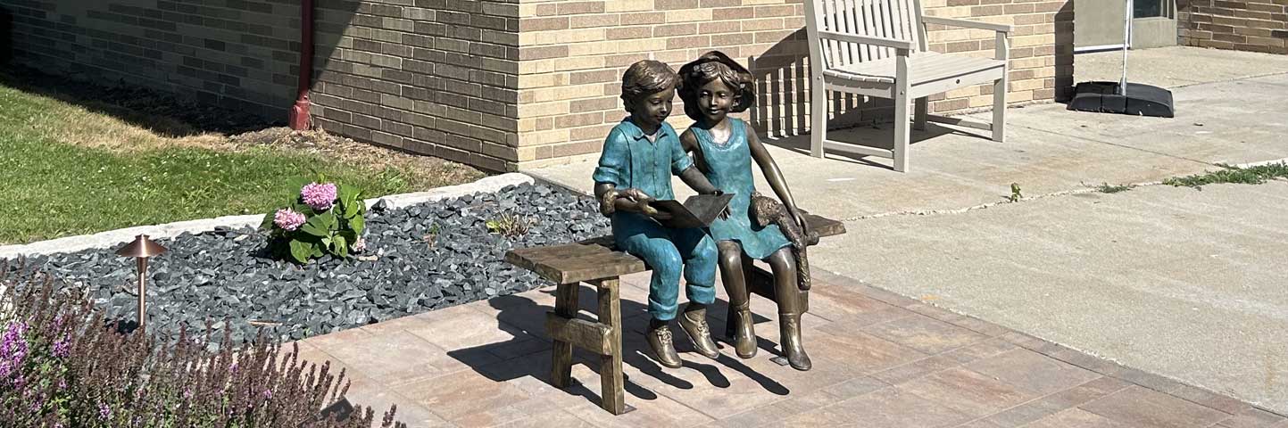 Statue of two children reading on a bench  outside library