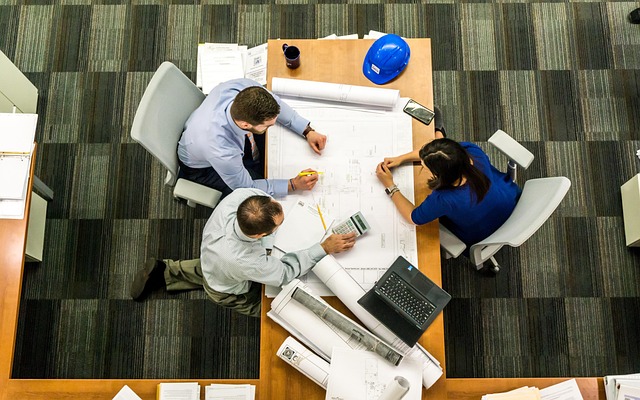 Arial view of three people meeting at a table containing blueprints.