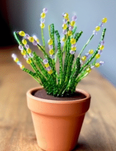 Terracotta pot containing plant made of green and yellow beads.