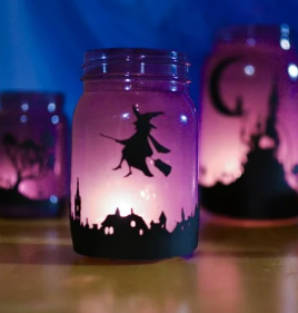 Glass votive holder with purple glow and witch riding on broomstick on side.